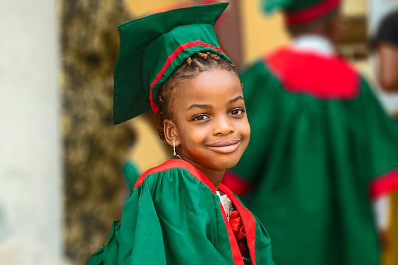 A smiling young girl in a green graduation gown and cap