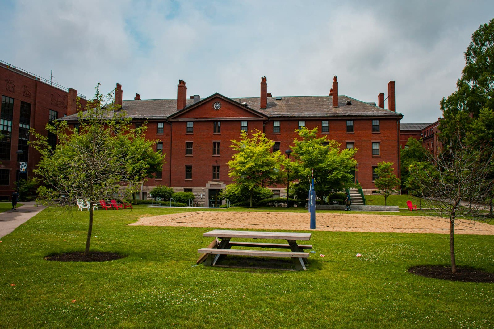 A red-brick school building behind a green lawn and young trees