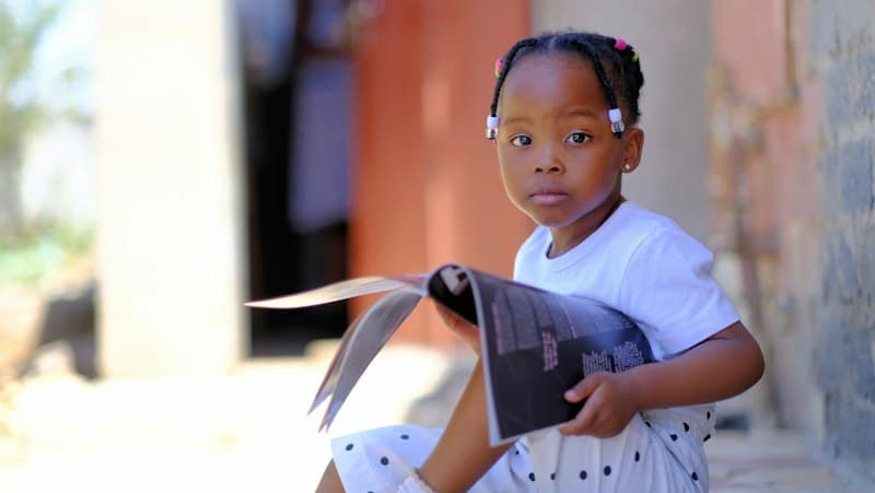 A young girl sitting outdoors and holding an open picture book