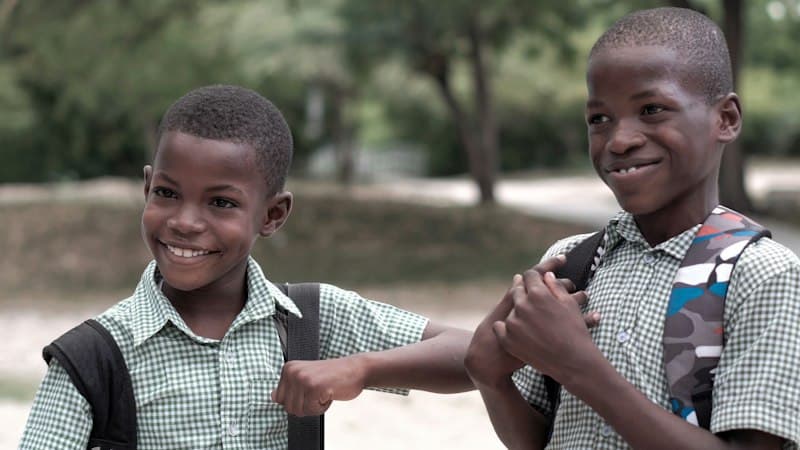 Two smiling primary school boys in checked uniforms with school bags