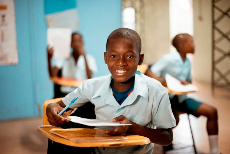 A smiling pupil in uniform writing at his desk
