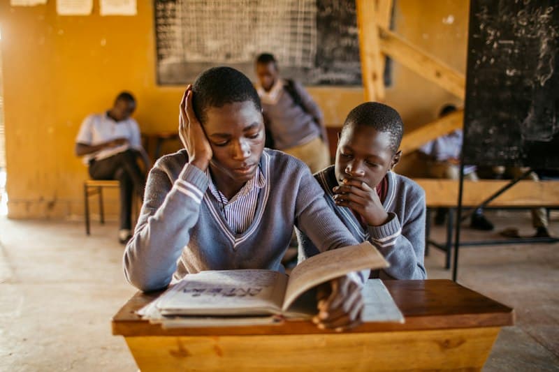 Two senior students reading a textbook together at a wooden desk